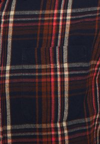 Koszula w kratę w ciemnogranatowych, czerwonych i beżowych odcieniach. Posiada przednią kieszeń, miękką fakturę i regularny krój.