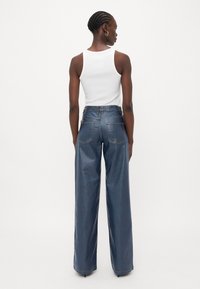 Hoge taille wijde jeans in donkerblauwe denim, met achterzakken en contrasterende stiksels, gecombineerd met een effen witte tanktop.