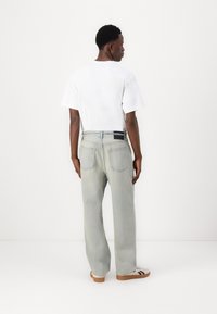 Lysblå denimjeans med en afslappet pasform, der har baglommer og et sort mærke på taljen. Sættes sammen med en simpel hvid t-shirt.
