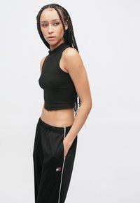 Čierny krátky tielkový top s vysokým golierom, kombinovaný s čiernymi teplákmi s bielymi bočnými pruhmi a malým logom na nohavici.
