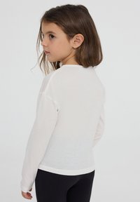 T-shirt a maniche lunghe in cotone beige chiaro, con scollatura rotonda e polsini a coste, dal taglio rilassato e dal morbido tessuto.