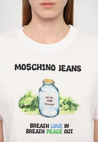 Hvit bomull t-skjorte med teksten "MOSCH1NO JEANS", et glassgrafikk med etikett, og fargerik tekst: "BØRSTE KJÆRLIGHET INN, BØRSTE FRED UT."
