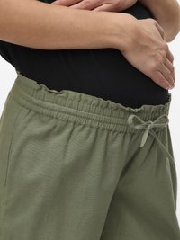 Manos descansando suavemente sobre un abdomen que lleva una camiseta negra y pantalones con cintura elástica verde oliva y cordón ajustable.