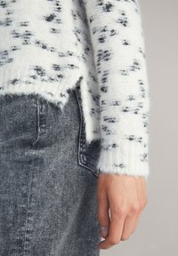 Maglione lavorato a maglia bianco e grigio con un motivo a macchioline, dotato di polsini a costine e orlo leggermente corto, abbinato a jeans grigio scuro.