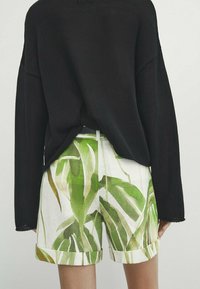 Czarny, dzianinowy sweter w oversize'owym fasonie, zestawiony z białymi szortami w zielony, liściasty wzór. Szorty mają podwinięty dół i luźny krój.