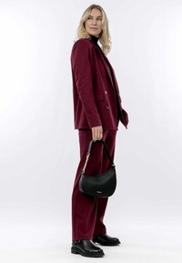 Bordeaux suit med en dobbeltbrystet blazer og lige ben bukser, parret med en lille sort læder håndtaske og kraftige sorte støvler.
