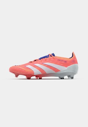 Chaussure de football rouge et blanche avec une tige texturée, un design courbé et une semelle grise. Comprend six crampons coniques pour l'adhérence.