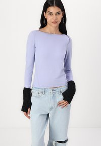 Light purple long-sleeved top with a boat neckline and ribbed black cuffs, paired with light blue distressed jeans. Smooth fabric texture.