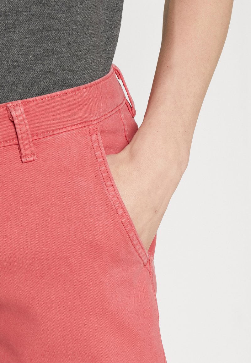 Pantalones de algodón rosa con cinturilla y detalles de bolsillo. La tela tiene una textura suave y se muestra combinada con una blusa gris.