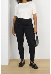 Jean slim taille haute noir en tissu de coton lisse. Associe à un haut blanc à manches courtes et des mocassins compensés noirs. Petit sac à main noir.