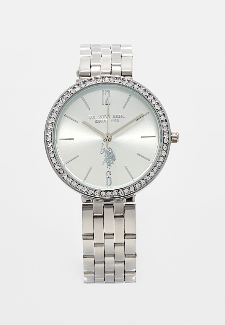 Montre-bracelet argentée avec un cadran rond, un bezel en cristal étincelant, un cadran minimaliste et un bracelet en métal à maillons. Présente le logo de U.S. Polo Assn.