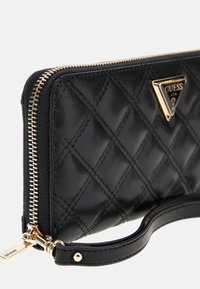 Black quilted wallet made of leather with a gold zipper and a gold triangle logo. Features a wrist strap for carrying convenience.