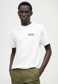 T-shirt en coton blanc avec un logo "Rip Curl" coloré sur la poitrine gauche. Manches courtes et col rond classique.