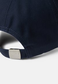 Gorra de béisbol Navy que presenta una tela texturizada, visera curvada y una correa ajustable de metal plateado con logotipo grabado.