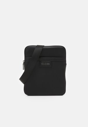 Czarna syntetyczna torba crossbody z zamkiem błyskawicznym, regulowanym paskiem i przednią naszywką z logo. Gładka tekstura, prostokątny kształt.