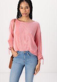 Top de rayas rojas y blancas de manga larga con un ajuste holgado, puños atados y cuello redondo. Combinado con unos jeans ajustados de color azul claro.