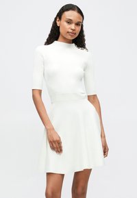 Vestido de punto blanco con un cuerpo ajustado de canalé, mangas cortas y falda acampanada. Presenta una cinturilla texturizada y acentos decorativos en los hombros.