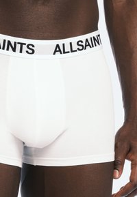 Vita boxershorts med en svart "ALLSAINTS"-logga på den elastiska midjebandet. Tyget ser slätt och åtsittande ut, med en design på frampanelen.