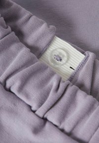 Lyse lilla stoff med rynket tekstur, med en hvit ribbestrikket linning og en klar knapp med blomstermønster.