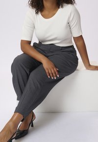 Haut blanc à rayures et manches courtes associé à un pantalon tailleur gris foncé. Le pantalon présente des jambes légèrement fuselées et des détails de couture à l'avant. Chaussures à talons noires.