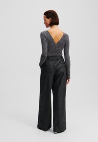 Zwart en zilver gestreepte wijde broek gecombineerd met een grijze sprankelende V-hals lange mouwen top. Gelaagd stof met een aansluitend ontwerp.