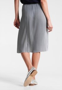 Raidallinen midi-hame, jossa on poimuttava muotoilu ja pystysuorat mustat ja valkoiset raidat. Yhdistettyinä hopeisiin kenkiin, sileä pinta, joustava vyötärö.