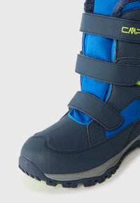 Zils tekstila un sintētisks necaurlaidīgs zābaks ar Velcro siksnām, gumijas zolēm un polsterētu apkakli, paredzēts aukstam laikam un āra aktivitātēm.