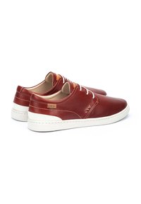 Zapatos deportivos rojos de cuero con una superficie texturizada, suela de goma blanca y detalles de cuero en contraste. Presenta cordones blancos y detalles del logo.