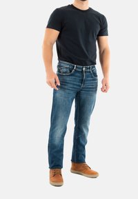 Vaqueros de mezclilla azul con corte recto, que presentan un diseño de cinco bolsillos y costuras visibles, combinados con una camiseta de cuello redondo negra y botas de color marrón claro.
