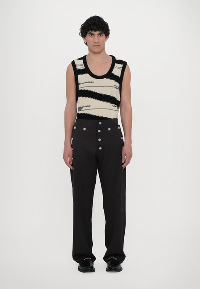 Top de malha em forma de tanque com padrão zigzag em preto e creme, emparelhado com calças pretas de cintura alta com detalhes em botões prateados.