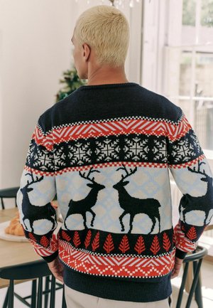 Knit sweater featuring a navy body with multicolored geometric patterns, reindeer motifs, and red leaf accents at the hem and cuffs.