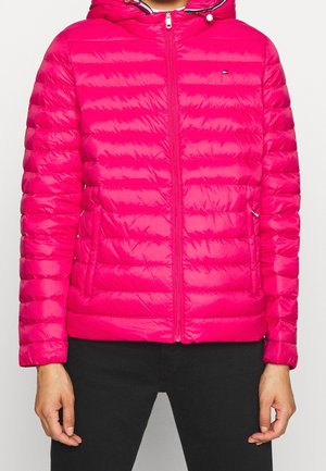 Felroze doorgestikte jas met capuchon, ritssluiting aan de voorkant, zijzakken, gedragen door een persoon in zwarte broek tegen een effen achtergrond.