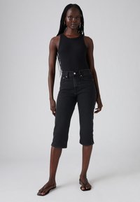 Sorte denim korte jeans med høy midje, fem lommer og rå kant. Kombinert med en svart ermeløs topp og svarte flip-flops.