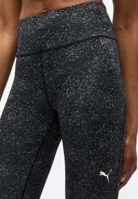 Κοντινό πλάνο ενός ατόμου που φοράει μαύρο και γκρι μαλακής υφής παντελόνι Puma με λευκό λογότυπο Puma στο αριστερό μηρό.