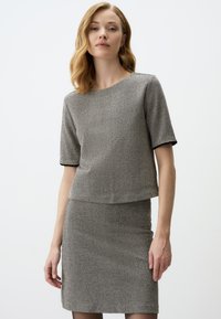 Ensemble deux pièces à chevrons gris comprenant un haut à manches courtes et une jupe cintrée. Le matériau a une finition texturée avec des accents en noir.