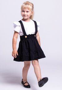 Czarna bawełniana sukienka z falbaną, regulowanymi ramiączkami i drewnianymi guzikami. W komplecie z białą koszulą z krótkim rękawem i czarnymi balerinami.