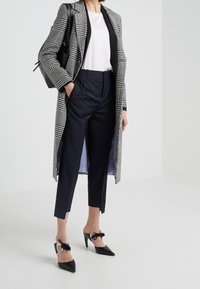 Sprawdzony długi płaszcz w czerni i bieli, zestawiony z granatowymi szytymi na miarę spodniami oraz czarnymi szpilkami z kokardką i okrągłymi akcentami.