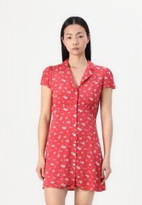 Rochie florală roșie cu mâneci bufante scurte, �închidere cu butoni și talie ajustată. Tesătura are flori mici albe pe un fundal luminos.