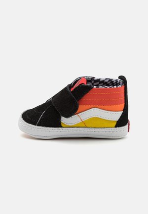 Chaussure à enfiler noire et multicolore avec une tige en daim, présentant des bandes horizontales rouges, orange et jaunes, des accents blancs, et une semelle texturée.