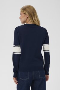 Námořnický modrý pletený svetr s bílými a námořnickými proužkovanými akcenty na rukávech. Žebrovaný límec a lem, střední tloušťka a hladká textura.