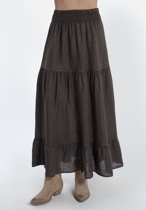 Gonna marrone a balze alla caviglia con vita elastica indossata con stivaletti beige in camoscio su sfondo bianco.