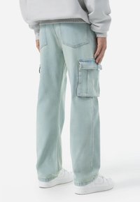 Lys blå denim cargo-bukser med en afslappet pasform, der har sidelommer og en let slidt tekstur. Matches med hvide sneakers.