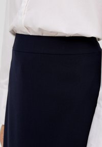 Knielanger, navyfarbener Rock aus glattem Stoff mit einem schlichten Bunddesign. Kombiniert mit einer weißen Bluse mit langen Ärmeln und weicher Textur.