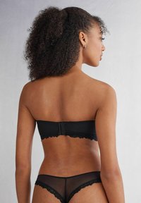 Soutien-gorge noir sans bretelles avec bordure en dentelle, fermeture à l'avant. Bas de bikini noir transparent avec détails en dentelle. Tissu lisse et design sans couture.