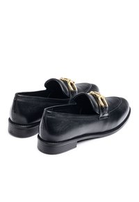 Black leather loafers with a low heel, featuring a gold-tone buckle detail on the front and smooth surface texture.