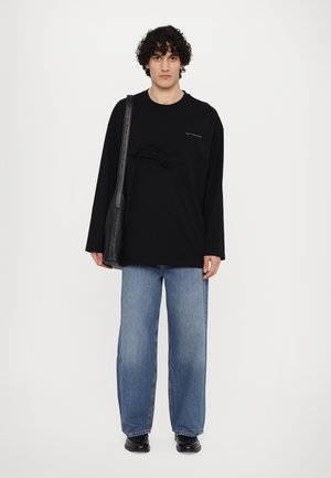 Oversized black long-sleeve shirt with textured panel, paired with loose light blue jeans. Black shoulder bag and black shoes complete the look.