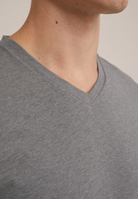 Tricou gri cu decolteu în V, confecționat dintr-un material moale și ușor. Are o textură netedă și o croială casuală, cu cusături vizibile de-a lungul gulerului.