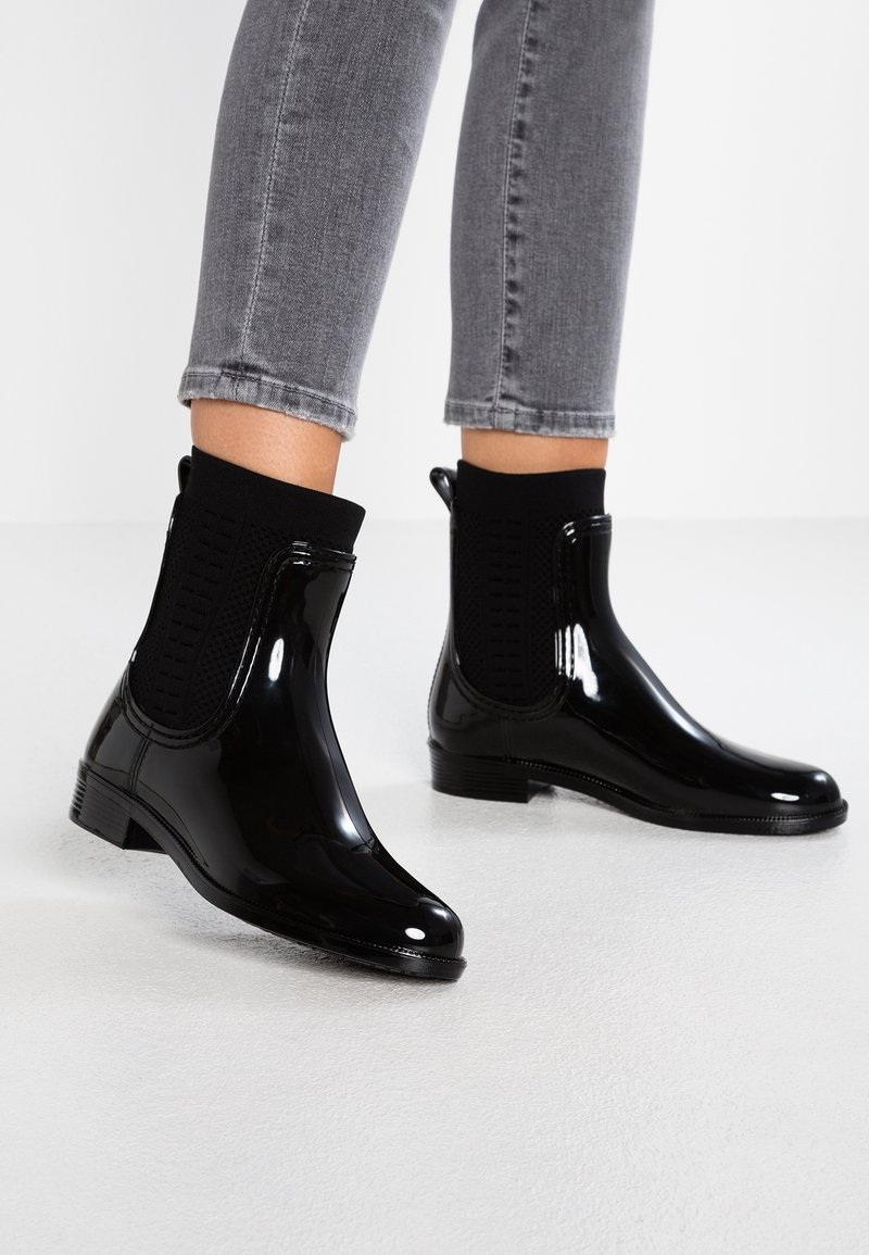Black glossy ankle boots with a smooth finish, elastic sock-like upper, and low heel. Textured side panels provide additional detail.
