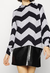 Sweat à capuche à manches longues gris et noir à motif chevron, coupe décontractée, associé à une mini-jupe noire brillante embossée crocodile.