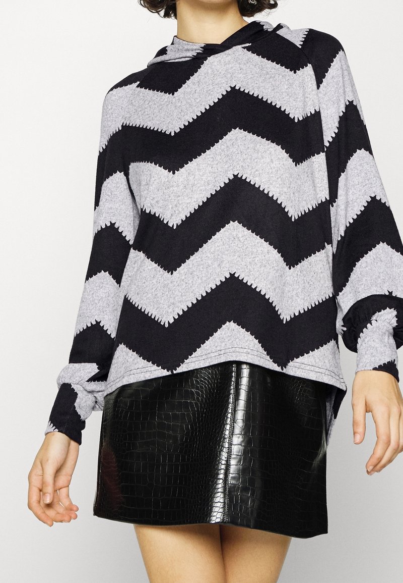 Sweat à capuche à manches longues gris et noir à motif chevron, coupe décontractée, associé à une mini-jupe noire brillante embossée crocodile.